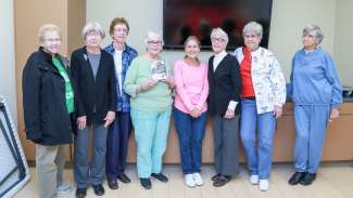 A group of active adults posing with a book recently read as part of a program 