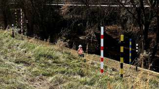 A woman jogs by a series of totem poles that represent several historic floodwater heights along Crabtree Creek