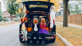 children with pumpkins sitting on a car trunk