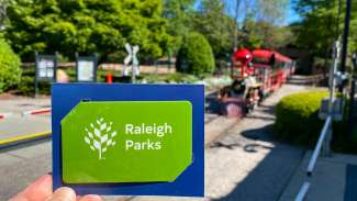 an image of a green Raleigh Parks gift card in front of train