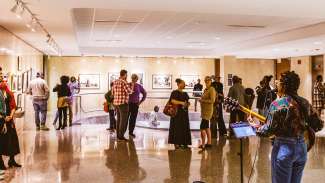 People gather in the Block Gallery for an artist reception. A musician plays the guitar for them.