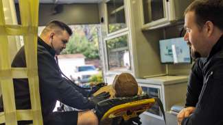 A firefighter listens to the heart of a training dummy with another firefighter looking on