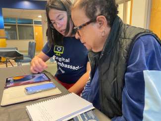 Volunteer and woman sit at table looking at iPhone device.