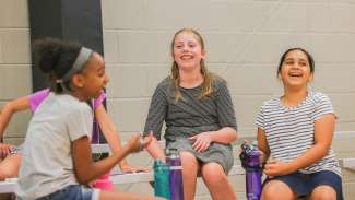 3 young students sitting on a bleacher while laughing