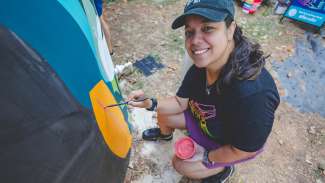 The artist smiling at the camera with paint in hand as she works on the cistern art.