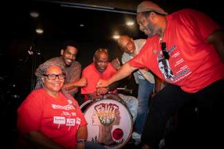 Four middle aged Black people excitedly smiling at each other and the camera after a music performance. 