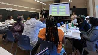 Photo of working group sitting at tables looking at presentation slide and speaker