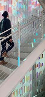 Modern stairway with light based artwork surrounding a woman walking up. 