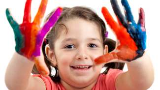 a smiling child with their hands messy with paint