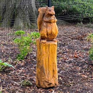 A wood carved squirrel sitting atop a carved tree stump.