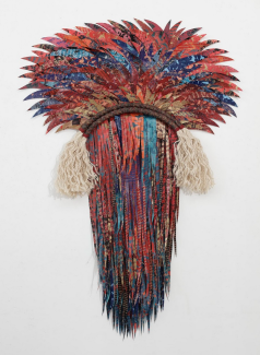 Two dimensional fiber sculpture with feather like fabric making a head-like shape in blues and reds. 