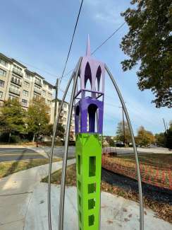 Purple and green tall, verticle metal scupture with window-like shapes. 